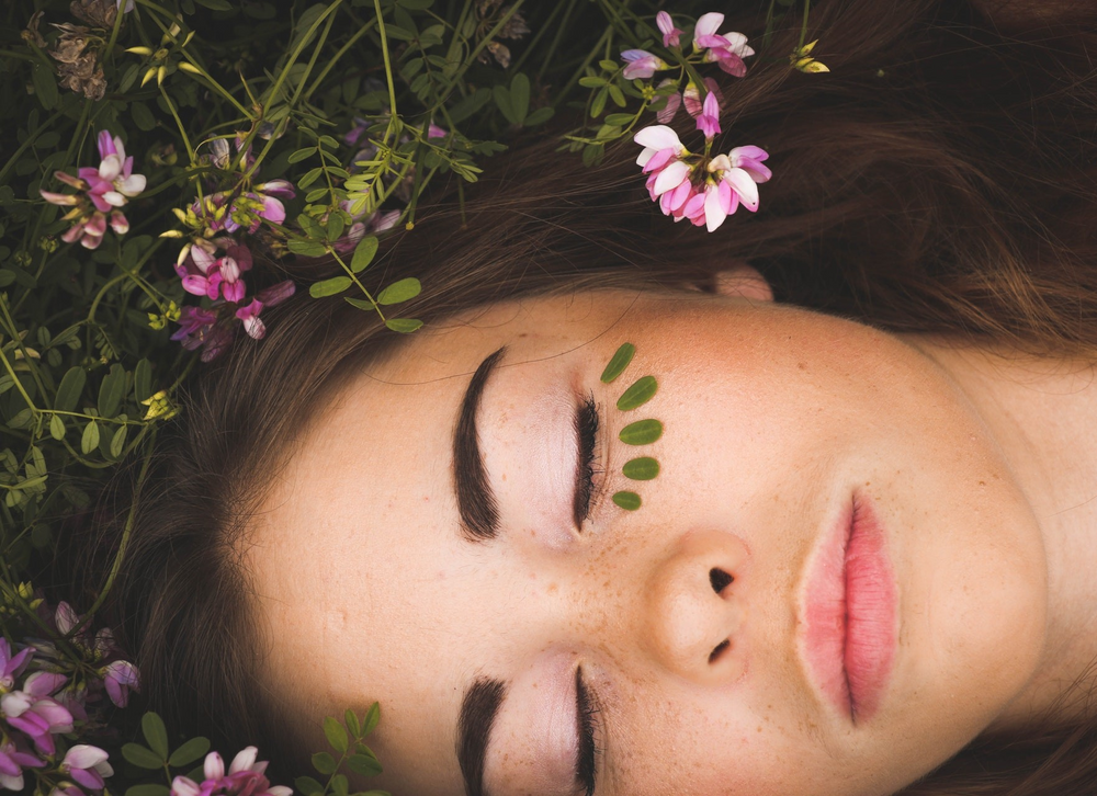 Natural beauty, header Bellaine. Voel je natuurlijke schoonheid, ontdek de kracht van de natuur. Natuurlijke, biologische, duurzame en veganistische verzorgingsproducten. Vrouw ligt in de natuur met blaadjes onder haar oog.